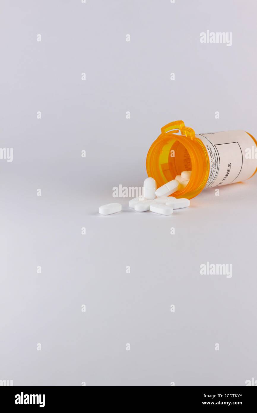 Pille Flasche liegt auf seiner Seite mit weißen Tablette Pillen Auf weißem Hintergrund mit Platz für die Kopie in auslaufen Hochformat Stockfoto