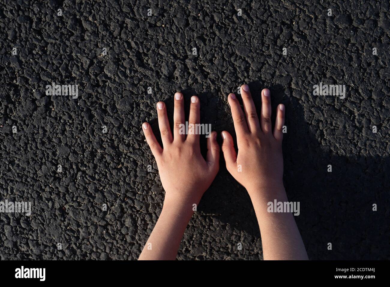 Kinderhände liegen auf schwarzer Straße, konzeptuelles Bild Stockfoto