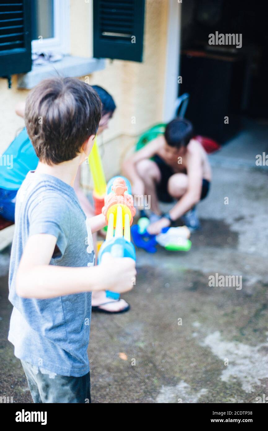 Kinder spielen im Garten mit Gewehren und Wassergewehren An einem sonnigen Sommertag Stockfoto