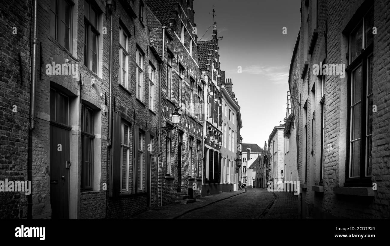 Schwarz-Weiß Foto einer typischen Kopfsteinpflasterstraße mit Backsteinhäusern in der historischen Stadt Brügge, Belgien Stockfoto