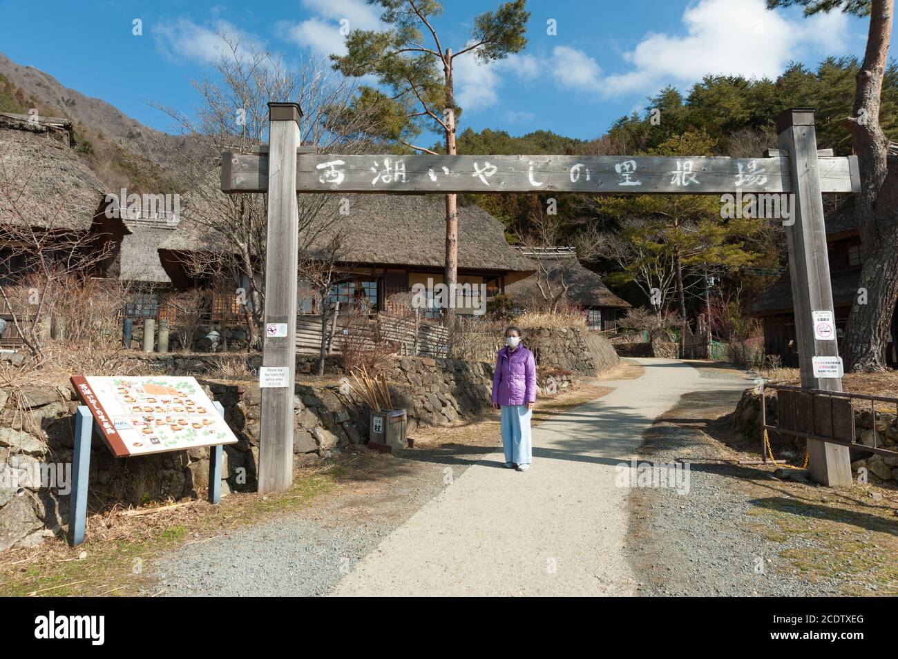 Frau mit einer chirurgischen Maske am Eingang des alten japanischen Dorfes Saiko Iyashino-Sato Nenba (Heildorf). Stockfoto