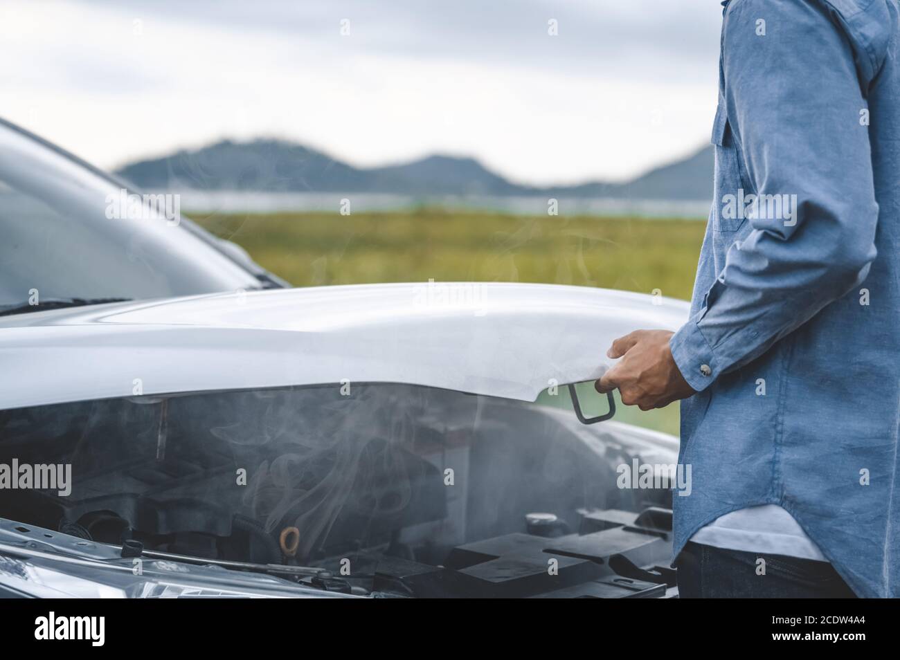 Asian Mann offene Auto Haube für die Reparatur als Wartung Service mit Landschaft Hintergrund zwischen langen Road trip. Auto gebrochen und Zusammenbruch in Mountain Meado Stockfoto