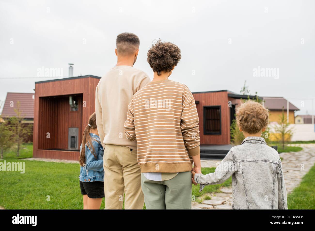 Rückansicht der Familie, die auf grünem Rasen im Freien steht Vor dem neuen Haus Stockfoto