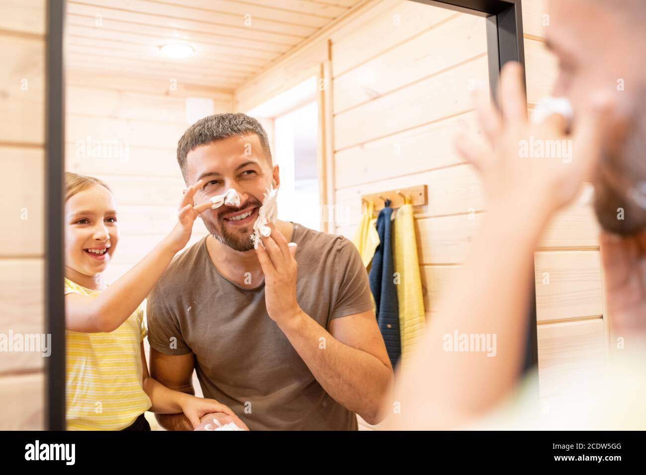 Junger fröhlicher Mann, der Schaum auf den Bart aufschäumt, während er im Stehen steht Spiegelvorderseite Stockfoto