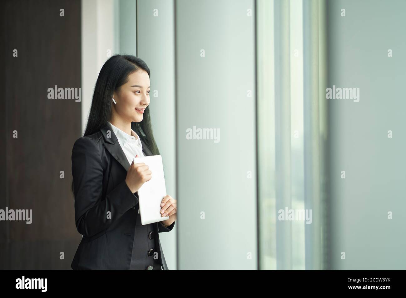 Junge asiatische Geschäftsfrau stehen am Fenster mit digitalen Tablet in Hand schaut heraus Stockfoto