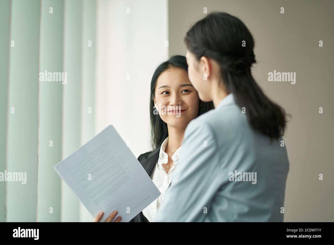 Zwei junge asiatische Geschäftsfrauen stehen am Fenster mit einem Diskussion im Büro Stockfoto