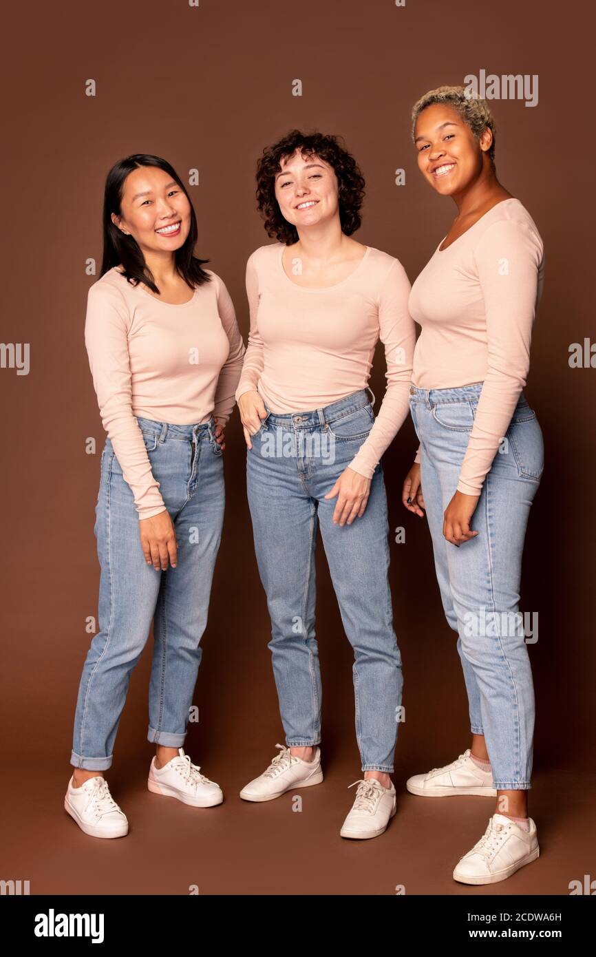 Drei junge interkulturelle fröhliche Frauen, die dich mit Toothy anguckend Lächeln Stockfoto