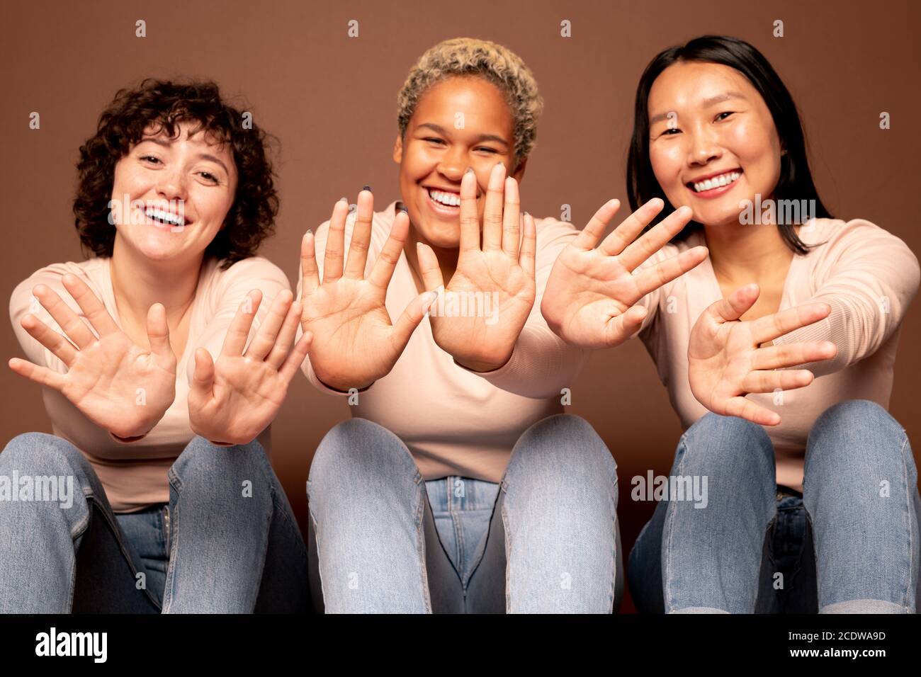 Fröhliche junge lächelnde Frauen verschiedener Ethnien, die ihre Handflächen zeigen Für Sie Stockfoto