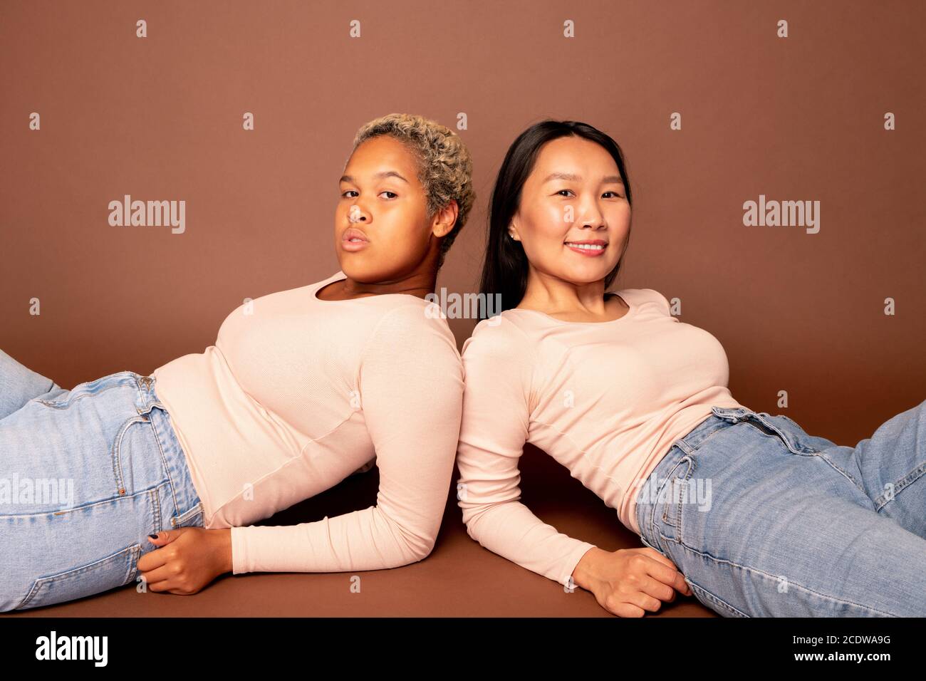 Zwei junge zeitgenössische Frauen verschiedener Ethnien liegen auf der Boden Stockfoto