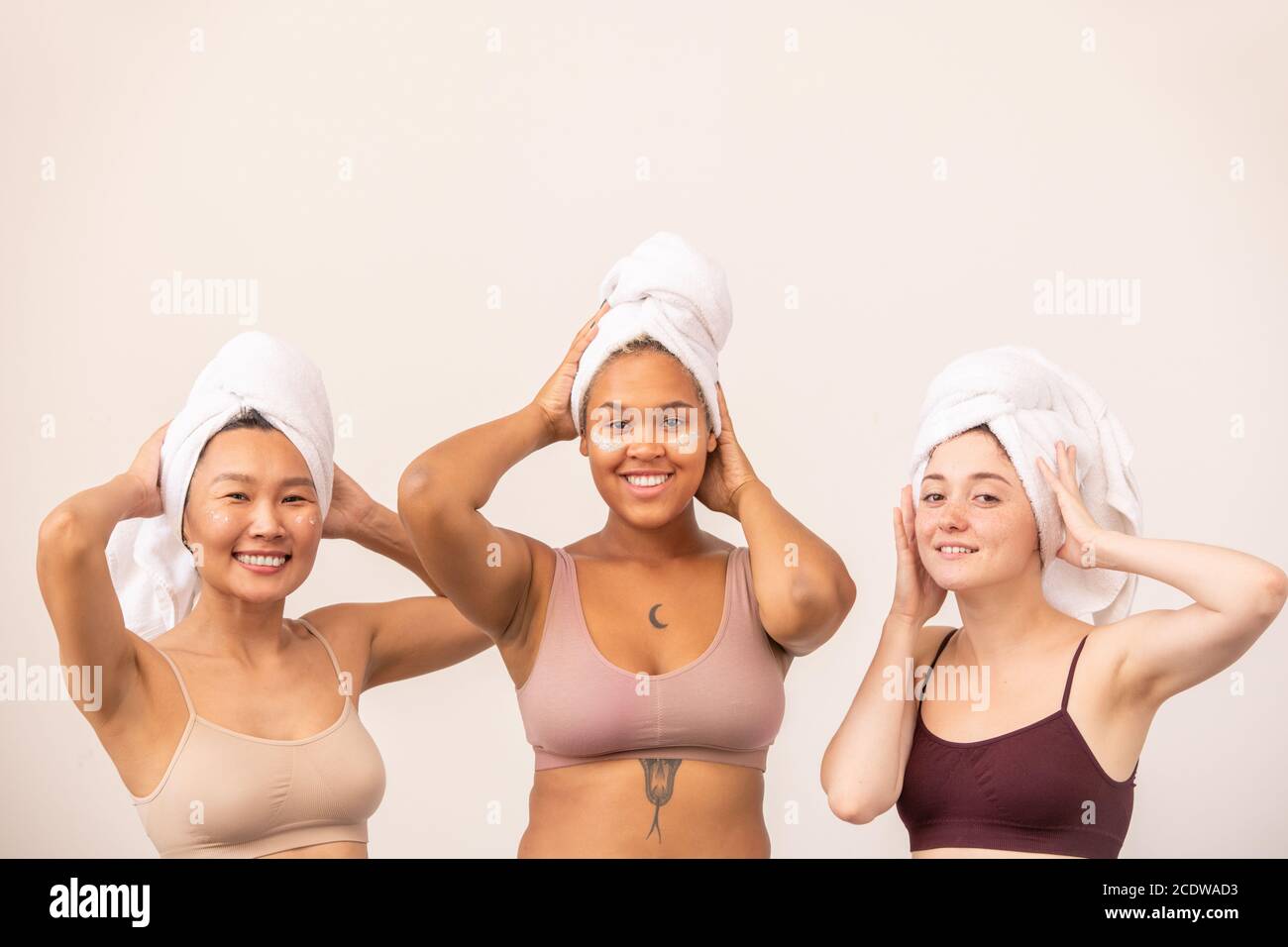 Junge glückliche asiatische, afrikanische und kaukasische Frauen mit weißen weichen Handtüchern auf den Köpfen Stockfoto