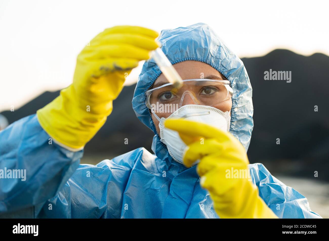 Junge Forscherin in schützende Arbeitskleidung Blick auf Kolben mit Probe Stockfoto