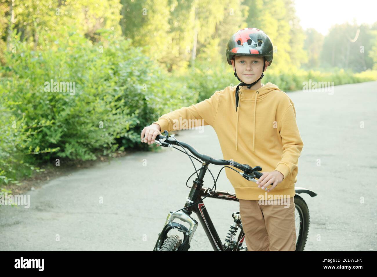 Jugendlicher Junge im Hoodie, beige Hose und Schutzhelm stehen mit Fahrrad Stockfoto