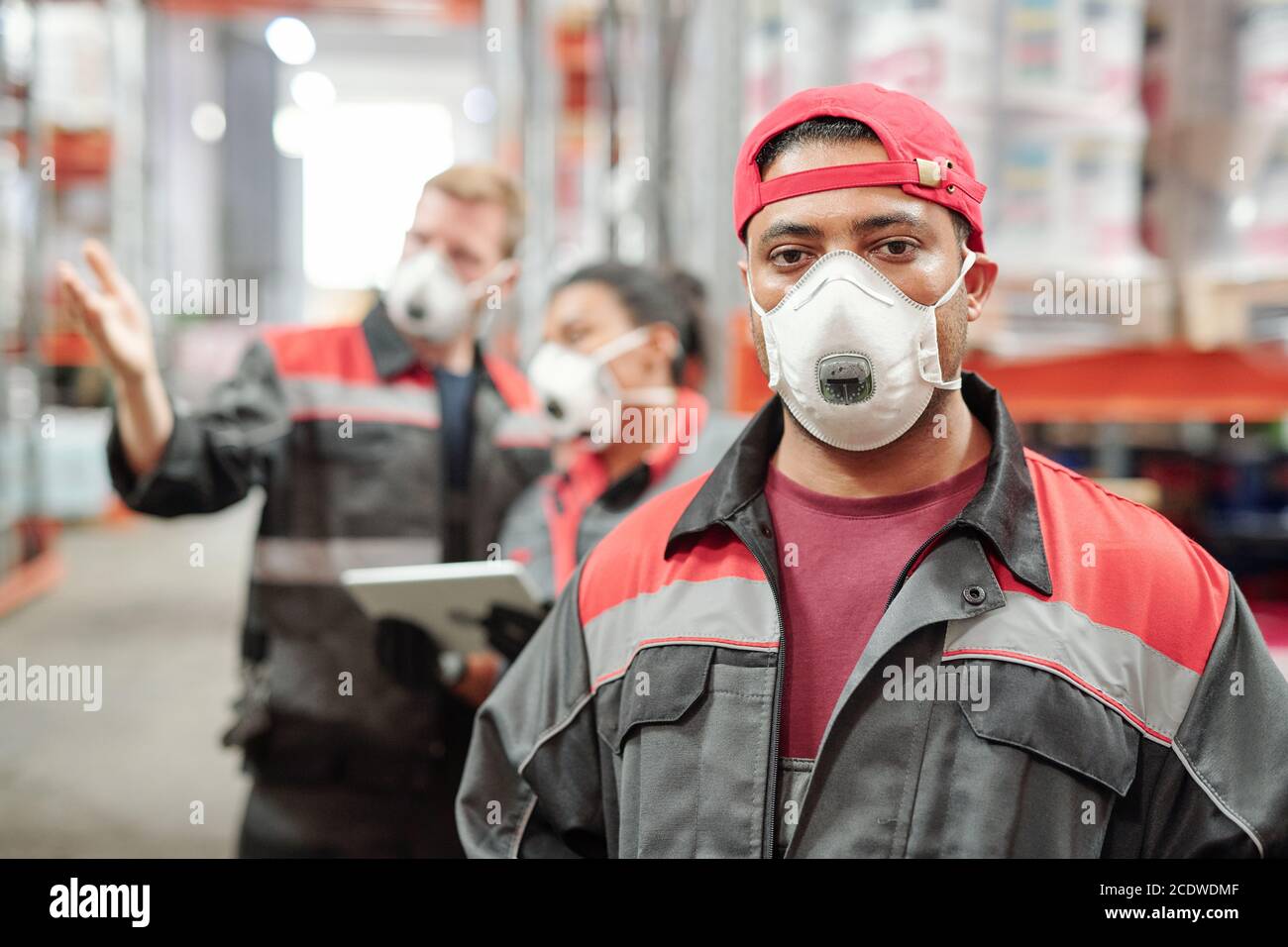 Latino Mann mittleren Alters in Arbeitskleidung und schützende Atemschutzmaske suchen Bei Ihnen Stockfoto