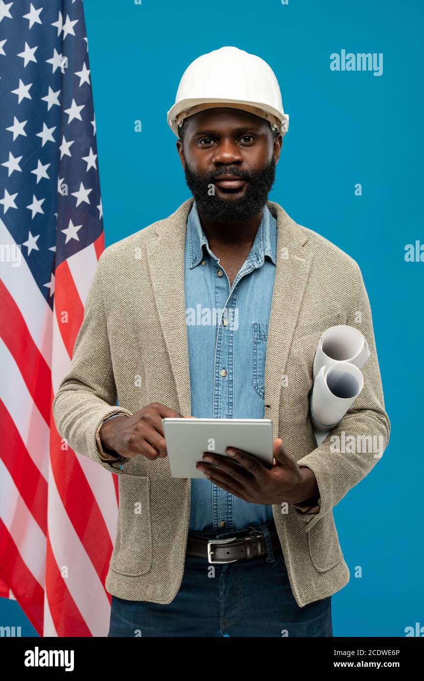Junger bärtiger afroamerikanischer Ingenieur mit Tablet und mit Blaupausen Stockfoto