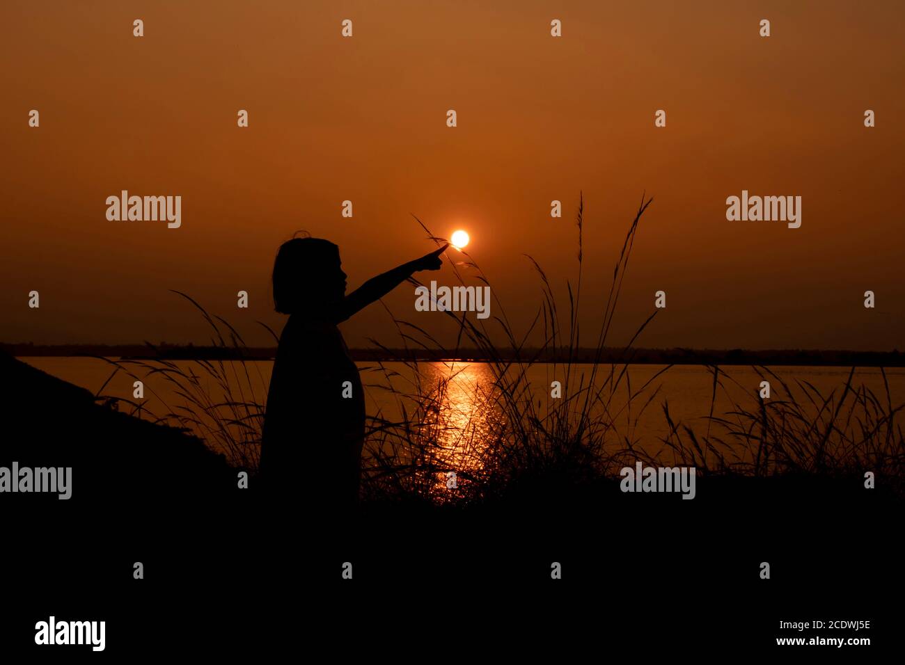 Am 5. Januar 2020 orange Silhouette Sonnenuntergang des Mädchens zeigen oder berühren Sonne auf bacreswar Damm, birbhum, West Bengalen, Indien Stockfoto