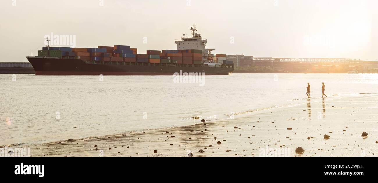 Großes Containerschiff und Stadtstrand an der Elbe in Hamburg bei Sonnenuntergang Stockfoto