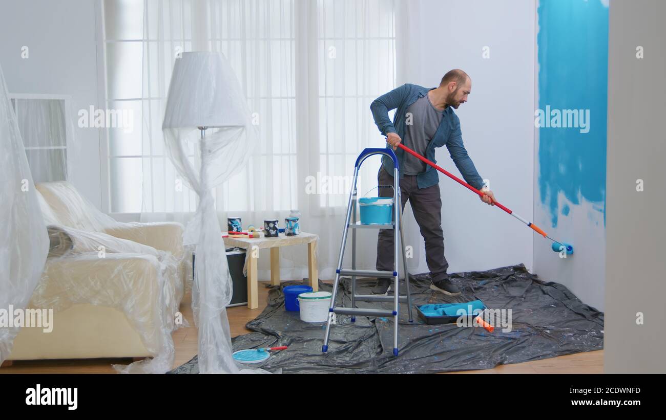 Junger Mann malte Wand mit Roller Pinsel während der Renovierung seiner Wohnung. Handwerker Renovierung und Hausbau während der Renovierung und Verbesserung. Reparatur und Dekoration. Stockfoto