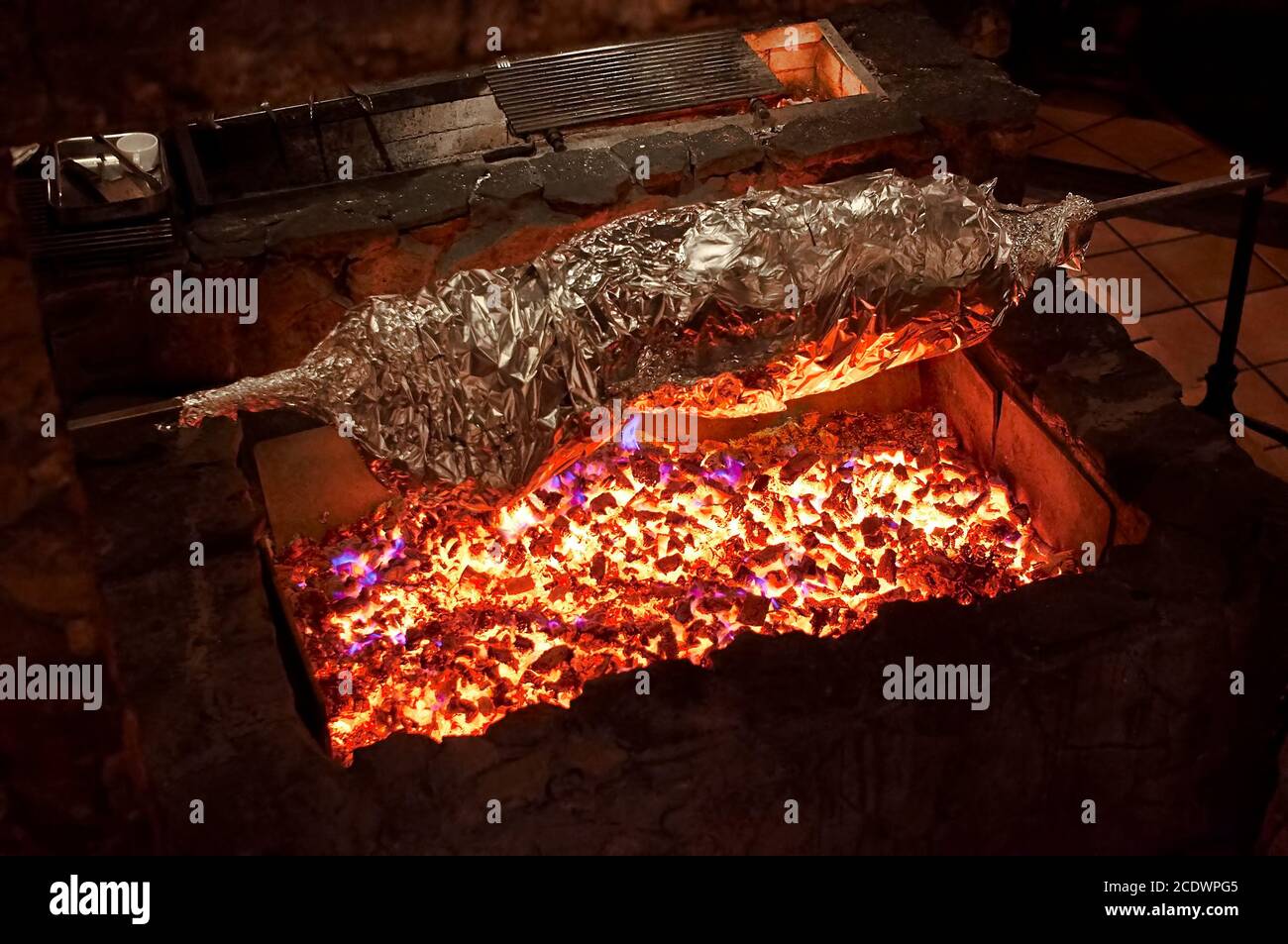 Gegrilltes Fleisch in Folie auf offenem Feuer. Ganzkörper Tier mit Folie auf einem großen Grill, Restaurant Küche gewickelt. Stockfoto