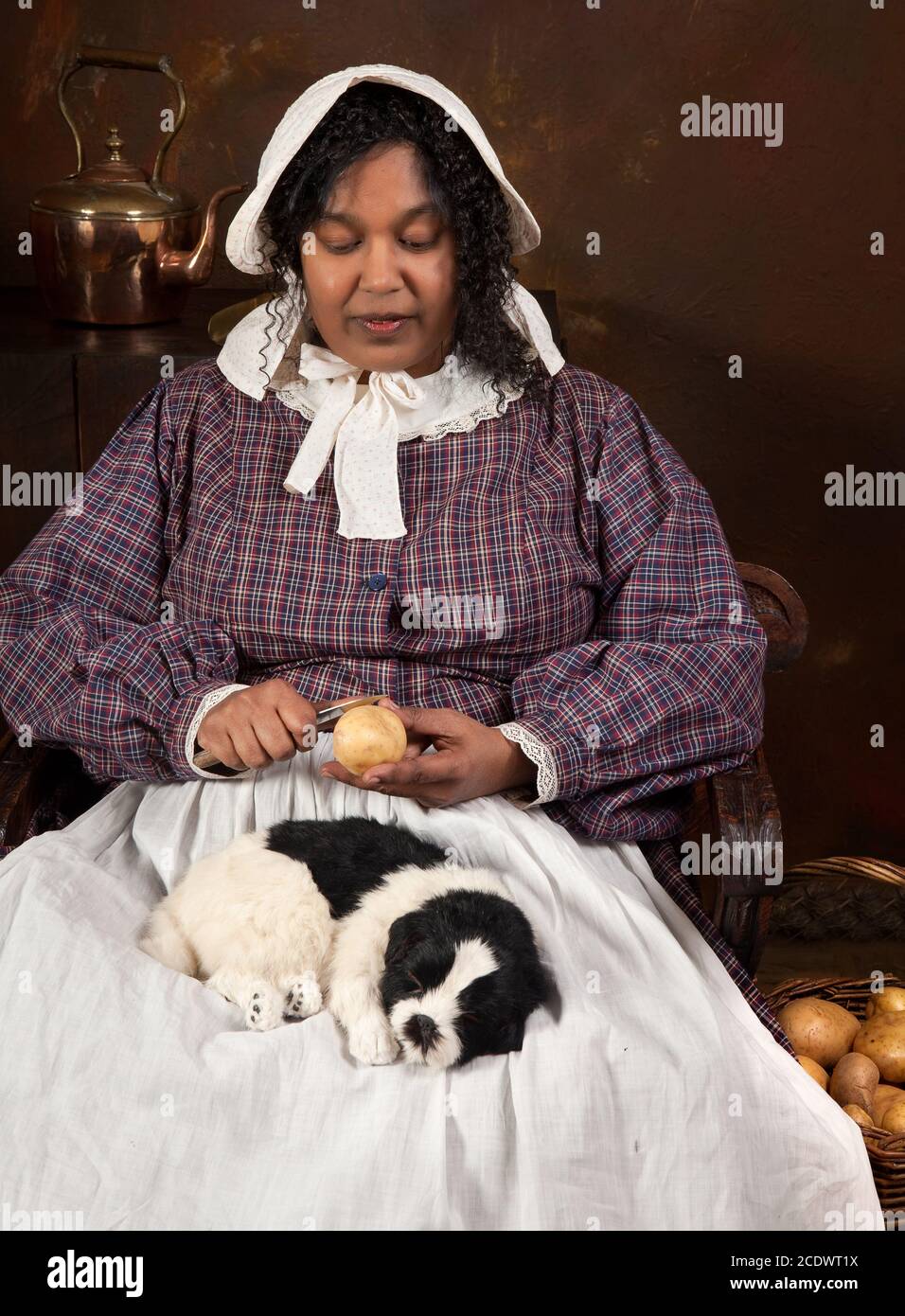 Reenactment-Szene eine schwarze viktorianische Maid Kartoffelschälen in eine antike Küche Stockfoto
