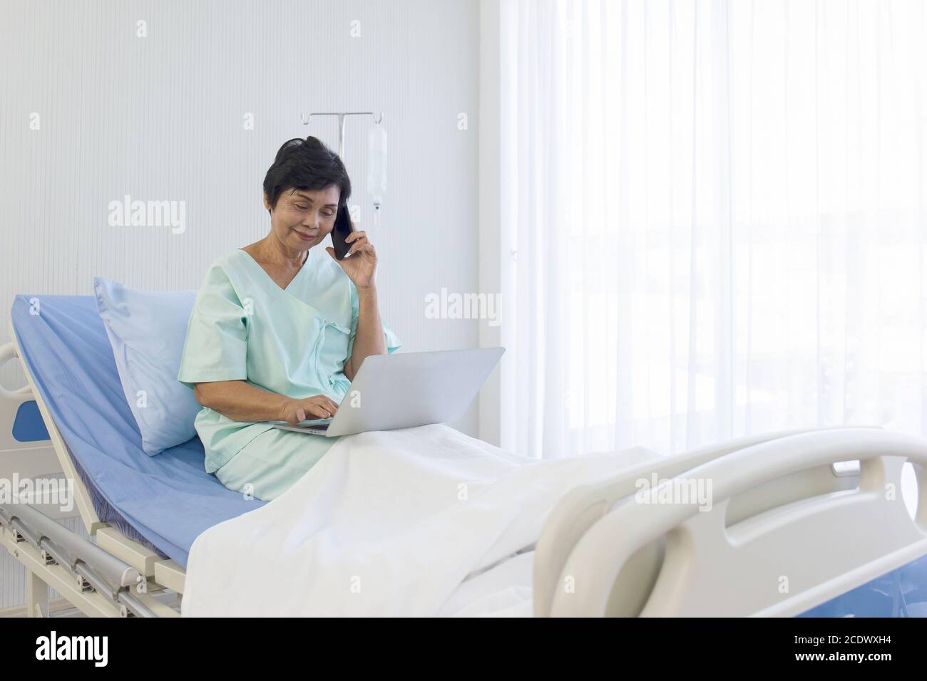 Die älteren asiatischen Frauen sitzen im Bett, erholen sich, sprechen am Telefon, und machen Besorgungen auf Laptops, in Krankenhäusern, Sonderzimmern. Stockfoto