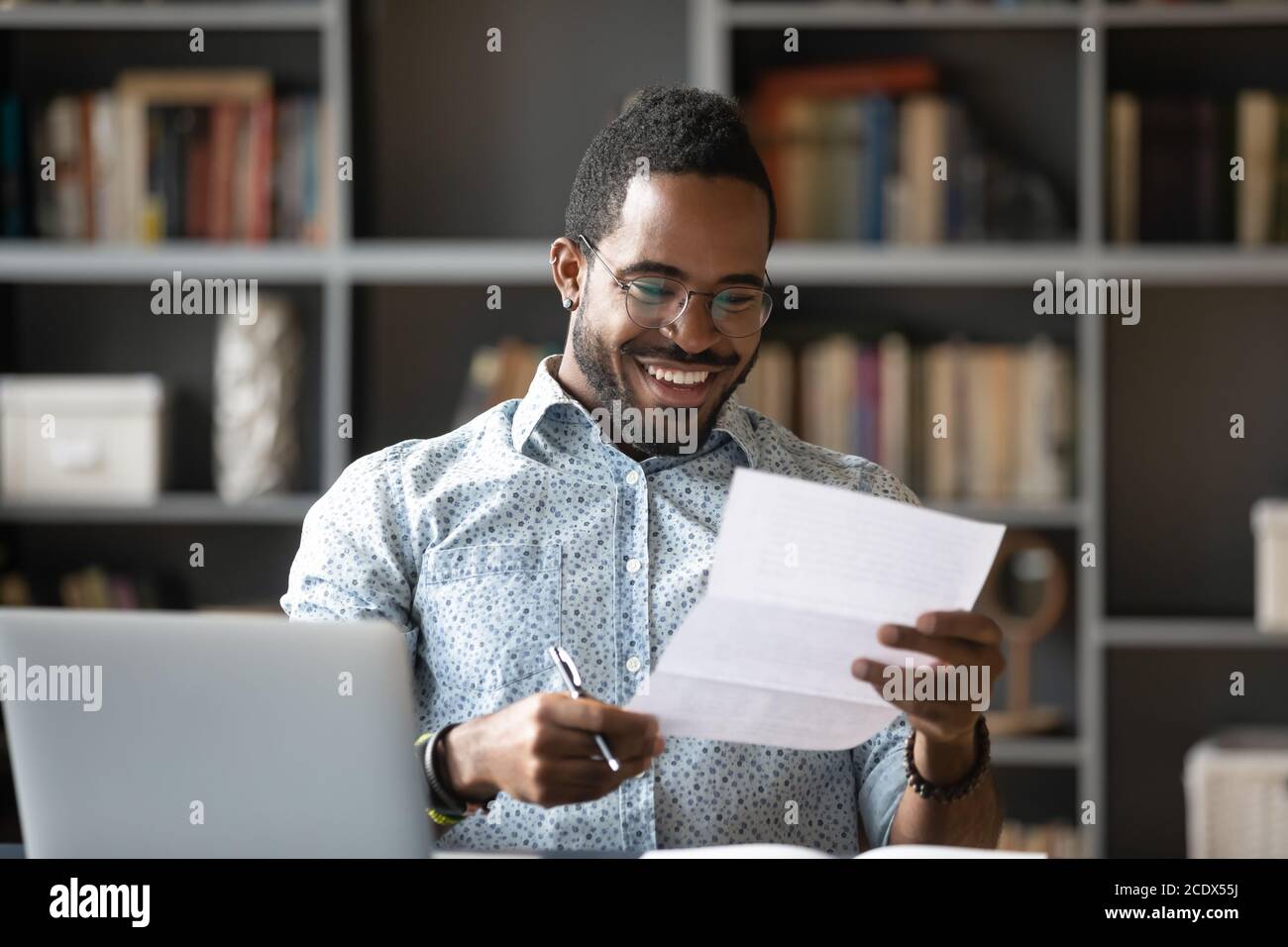 Glücklicher lächelnder afroamerikanischer Mann, der Brief am Arbeitsplatz liest Stockfoto