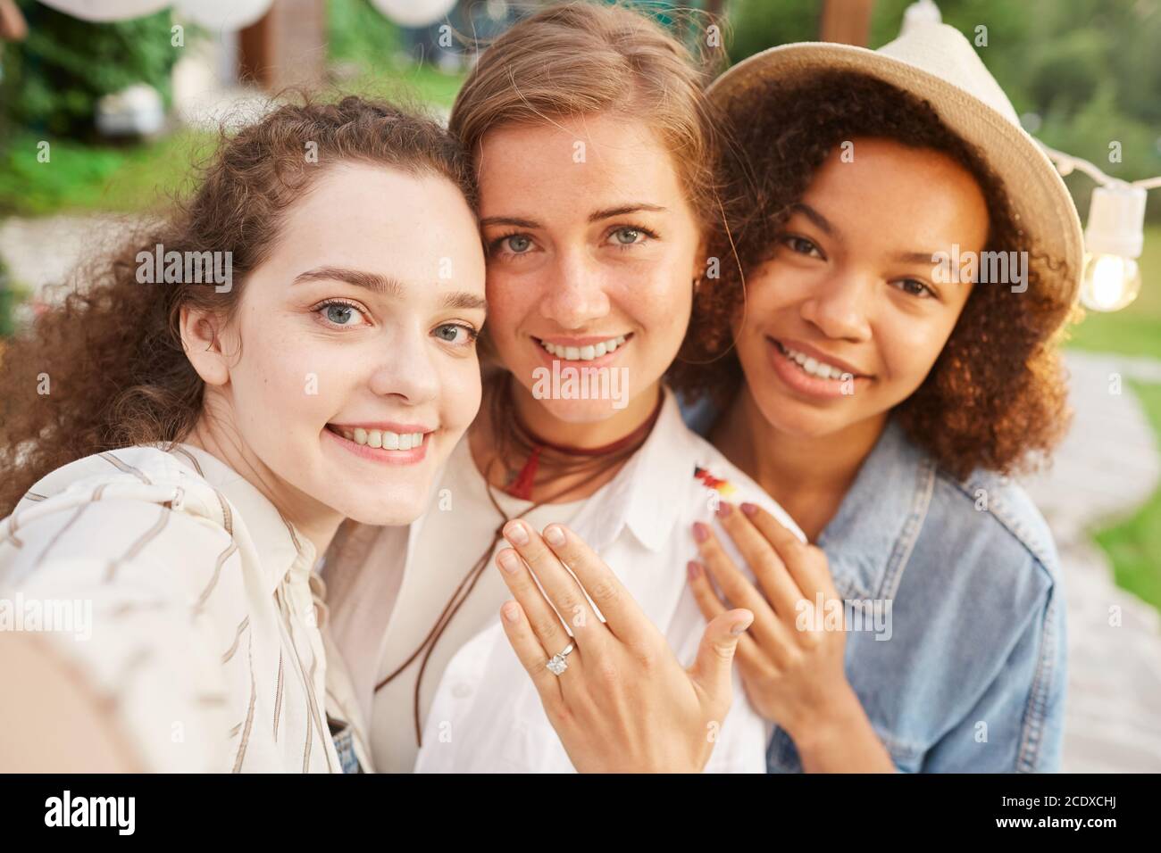 POV Porträt der schönen jungen Frau zeigt Verlobungsring nehmen Selfie mit Freunden während der Party im Freien Stockfoto