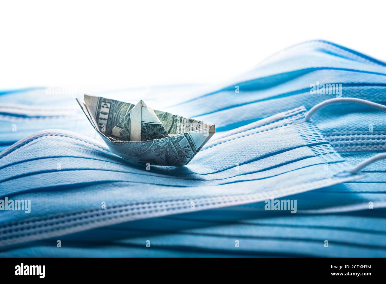Dollar wirft auf die Wellen. Finanzielle Probleme Konzept, Banknote Origami-Schiff mit chirurgischen Masken. Stockfoto