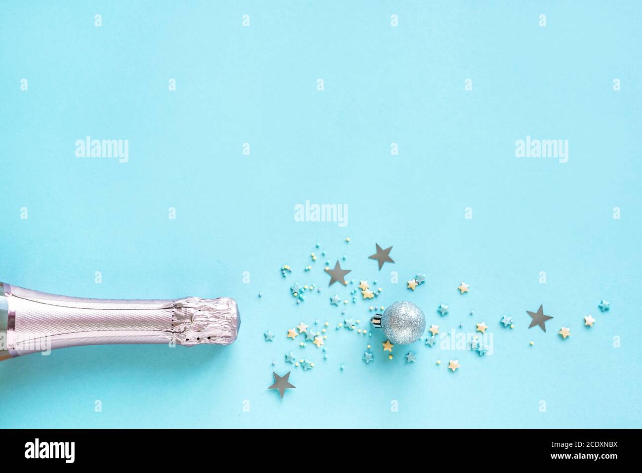 Weihnachtskomposition. Champagner-Flasche und silberne Konfetti Sterne und Kugeln auf blauem Hintergrund. Festliche flache Lay-Ansicht, Draufsicht, Kopierbereich. Stockfoto