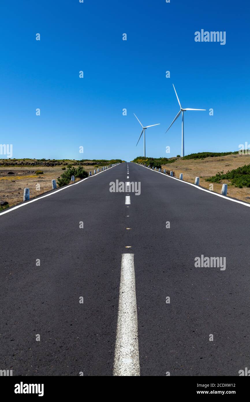 Eine gerade Straße mit zwei Windenergieanlagen über dem Bereich, der mit einem blauen Himmel Stockfoto