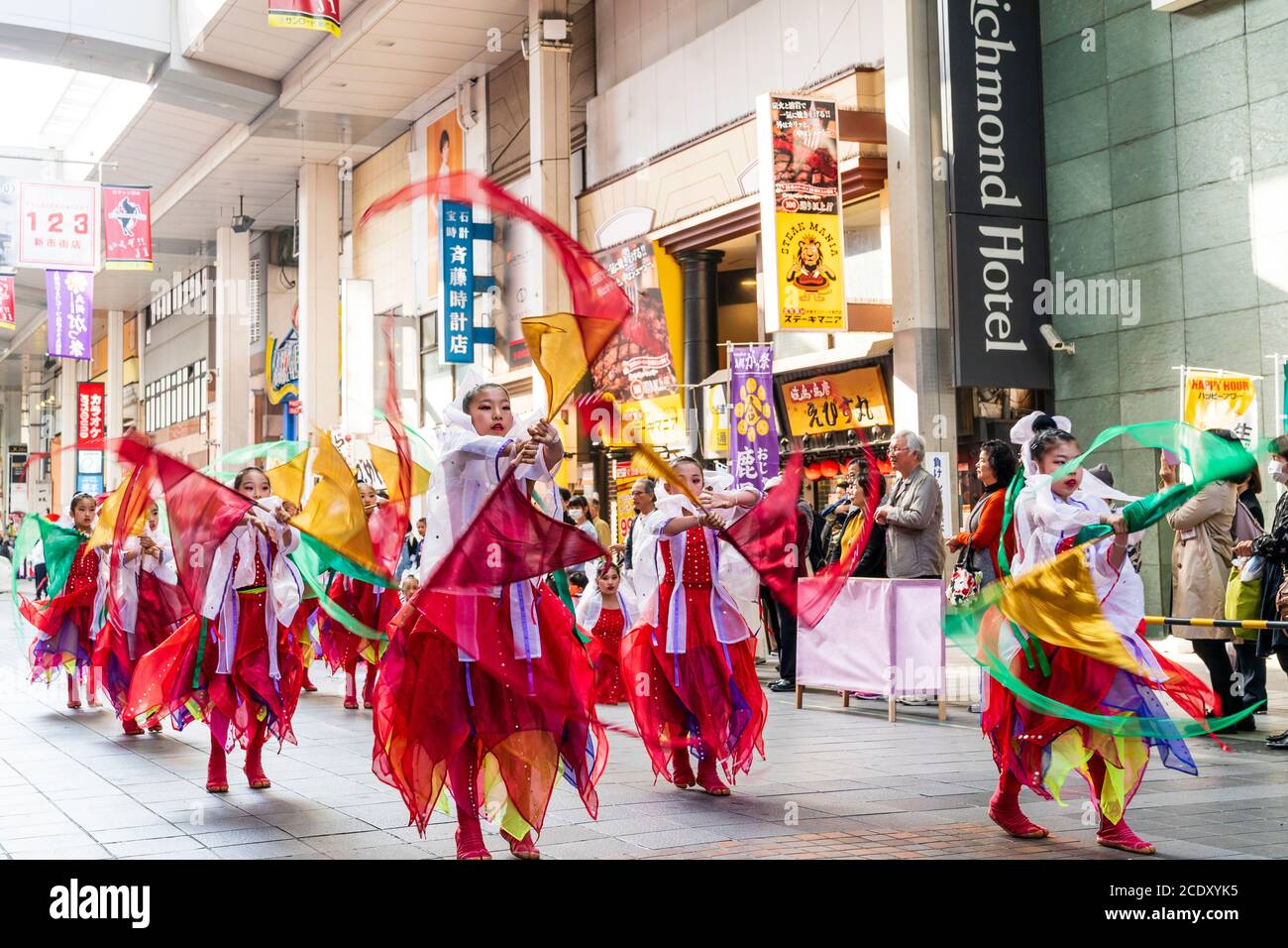 Japanisches Team von Kindern, 9-10 Jahre alt, yosakoi Tänzer tanzen in der Einkaufspassage und drehen um Kleidung am Ende der Stange. Bewegungsunschärfe. Stockfoto
