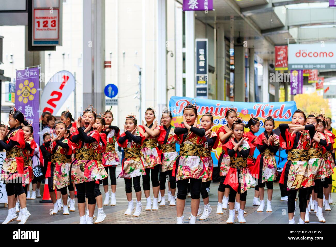 Team japanischer yosakoi-Tänzer, die während des Kyusyu Gassai Tanzfestivals in Japan mit Namensbanner hinter ihnen in einer Einkaufspassage tanzen. Stockfoto