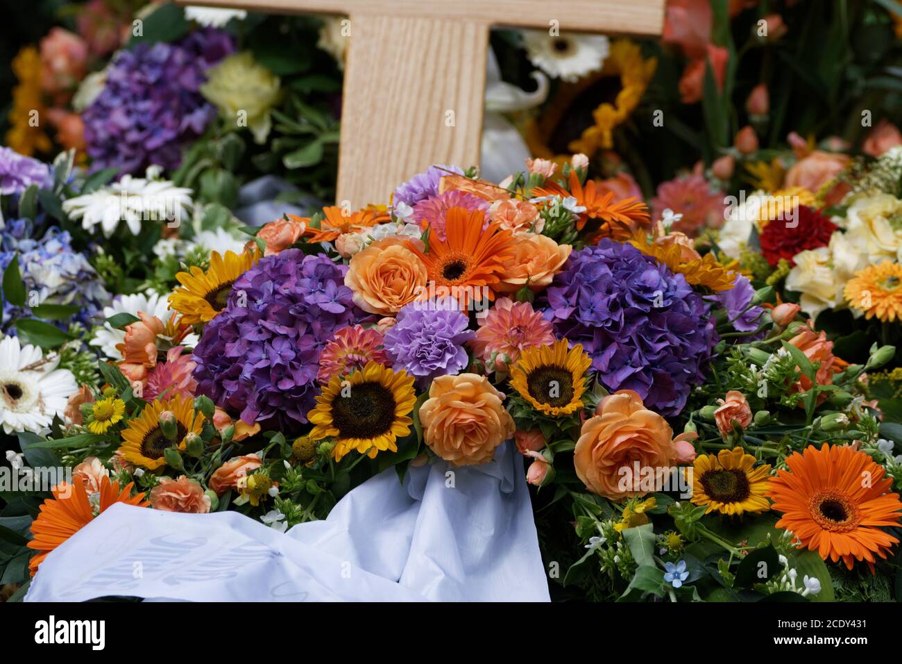 Blumen und Begräbniskränze auf einem neuen Grab mit wodden Kreuz Stockfoto