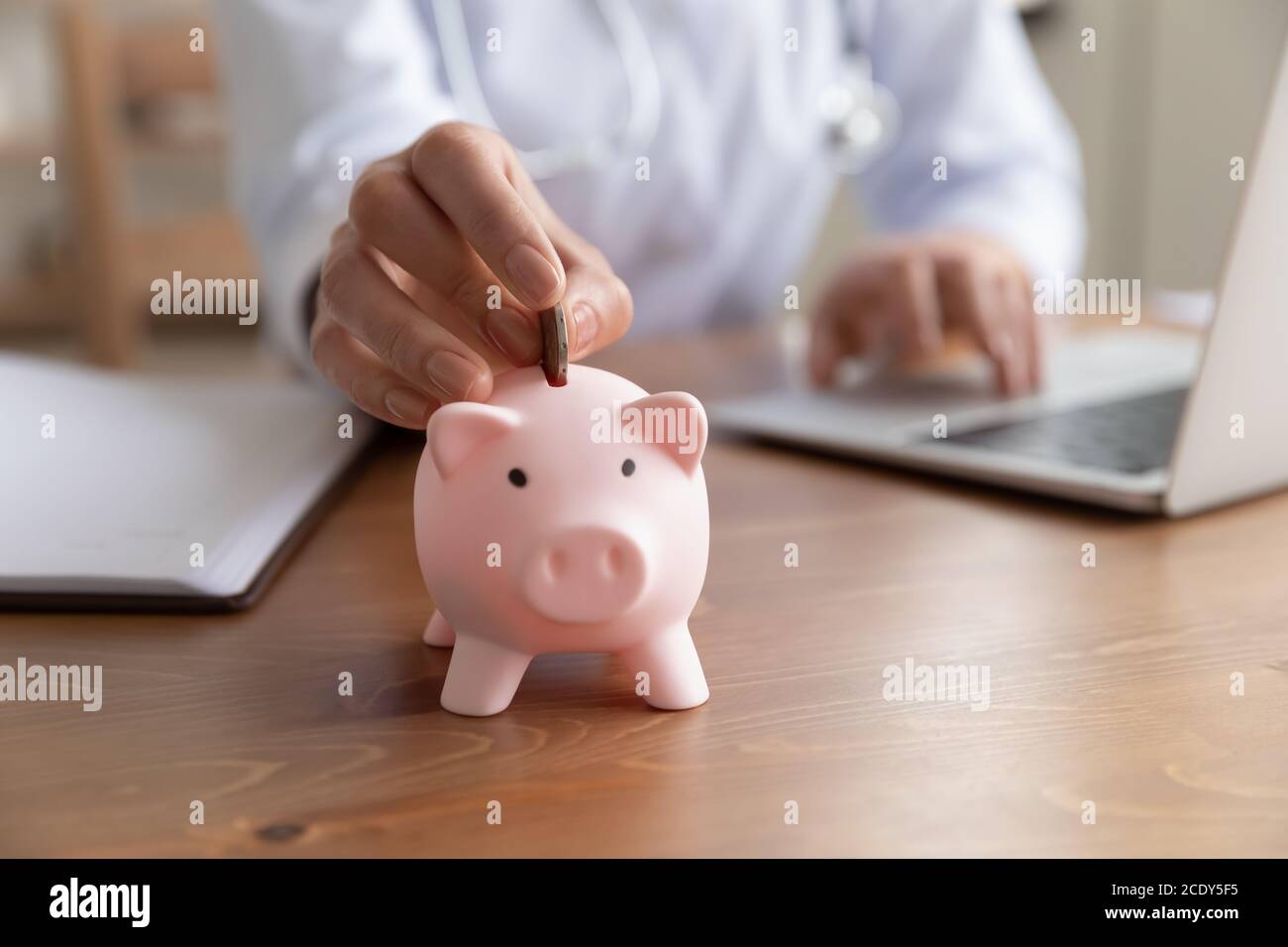 Nahaufnahme junge Frau Arzt Putting Münze in Sparschwein Stockfoto