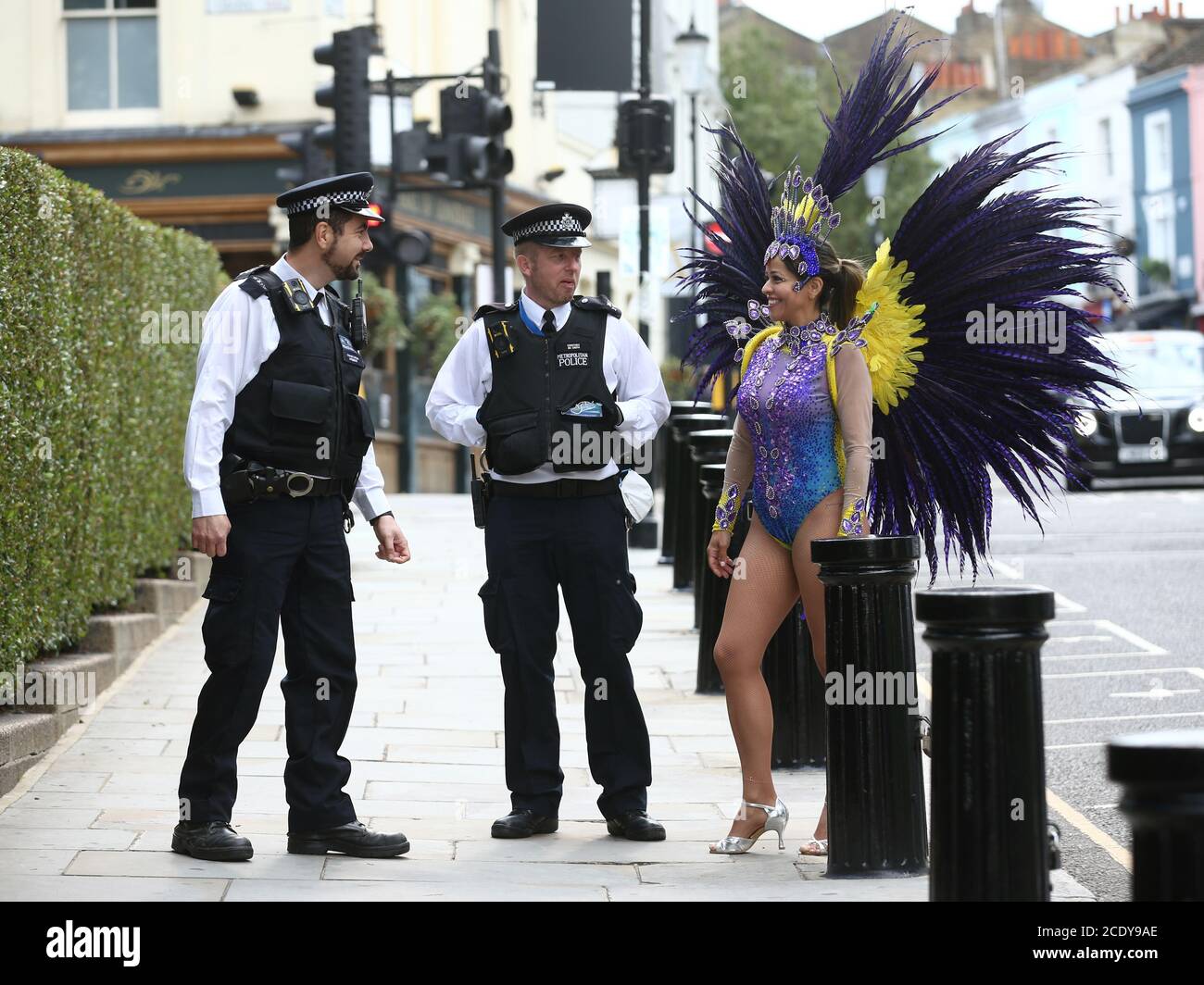 Polizeibeamte auf Patrouille unterhalten sich mit Pilates-Ausbilderin Juliana Campos, während sie in ihrem Karnevalskostüm in Notting Hill, London, auf dem Wochenende des Notting Hill Carnival posiert, nachdem der Karneval 2020 wegen der Coronavirus-Pandemie abgesagt wurde, Mit Veranstaltungen, die online gestreamt werden. Stockfoto