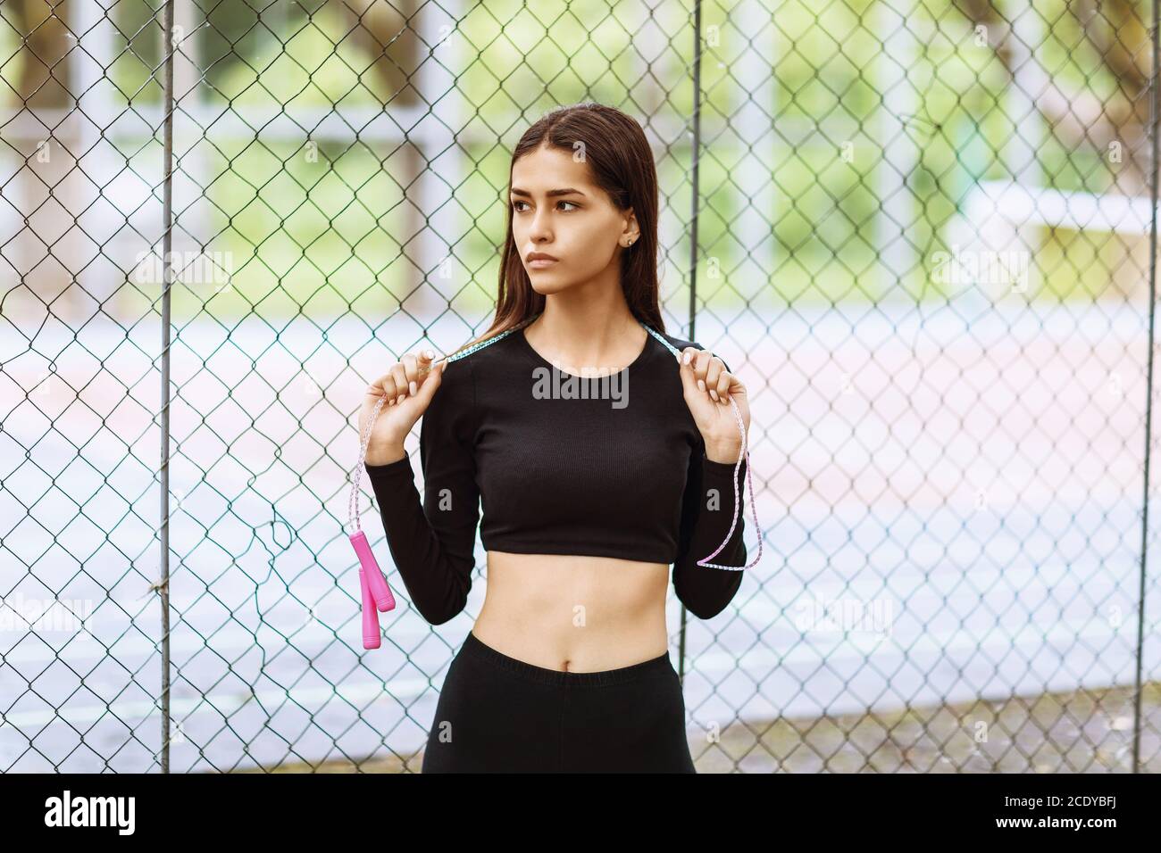 Porträt einer jungen Sportlerin mit Springseil In ihren Händen auf dem Hintergrund des Netzes in Der Park Stockfoto