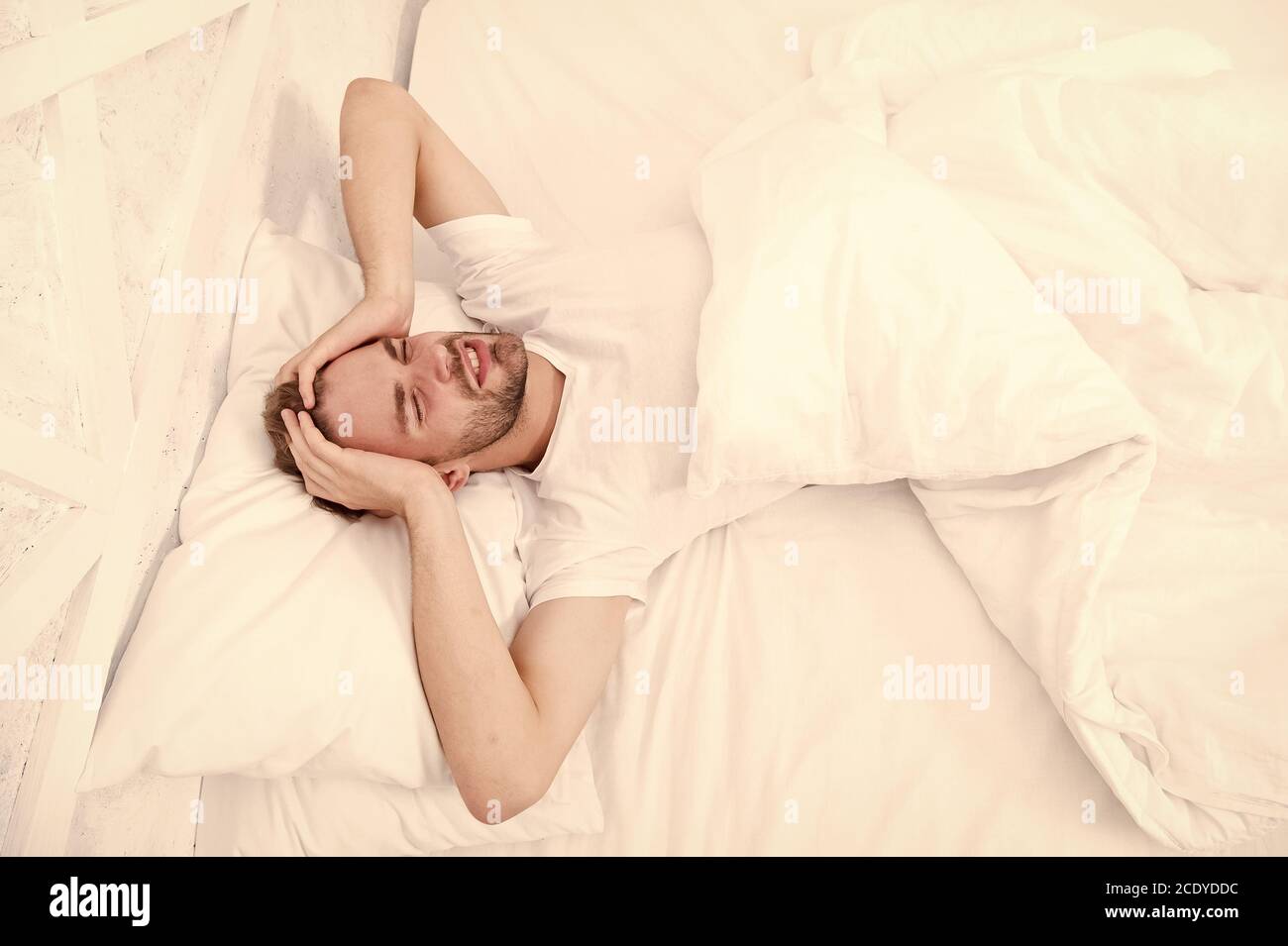 Schlafprobleme können morgens zu Kopfschmerzen führen. Gutaussehender Mann, der sich im Bett entspannen kann. Schnarchen kann zu erhöhten Risikopschmerzen führen. Häufiges Symptom der Schlafapnoe. Ursachen für Kopfschmerzen am frühen Morgen. Migräne-Kopfschmerzen. Stockfoto