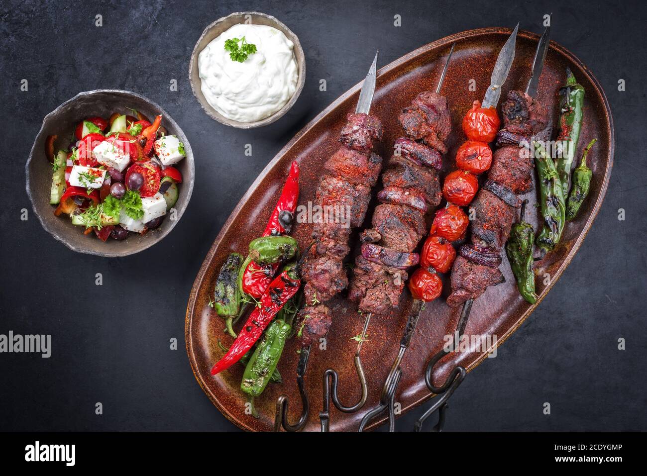 Traditioneller griechischer Souvlaki-Grillspieß mit Bauernsalat und Zatziki Als Draufsicht auf einem alten rustikalen Teller Stockfoto