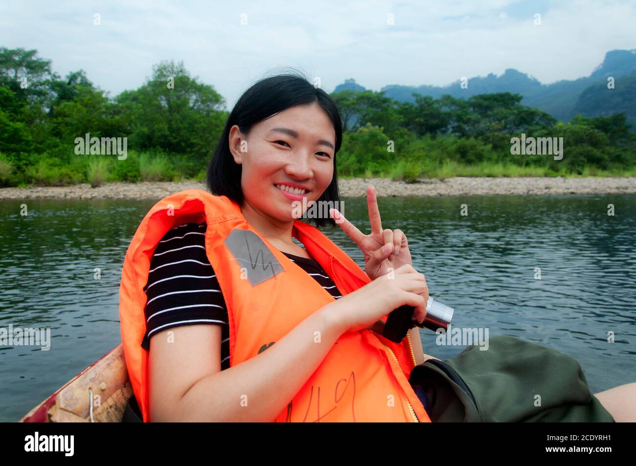 Eine chinesin, die ein Friedensschild mit einer Kamera zeigt Trägt eine orangefarbene Rettungsweste auf einem Bambusfloß Der neun Biegefluss in wuyishan china auf einem Überlauf Stockfoto