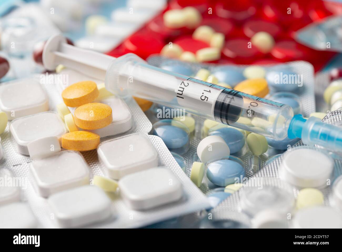 Medikamente und Einwegspritze, verschiedene Tabletten in verschiedenen Farben auf blauem Hintergrund. Stockfoto