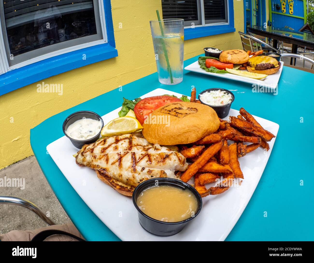 Fisch-Sandwich-Teller mit Süßkartoffeln Pommes mit Hambuger-Teller Im Hintergrund in farbenfroher Umgebung Stockfoto