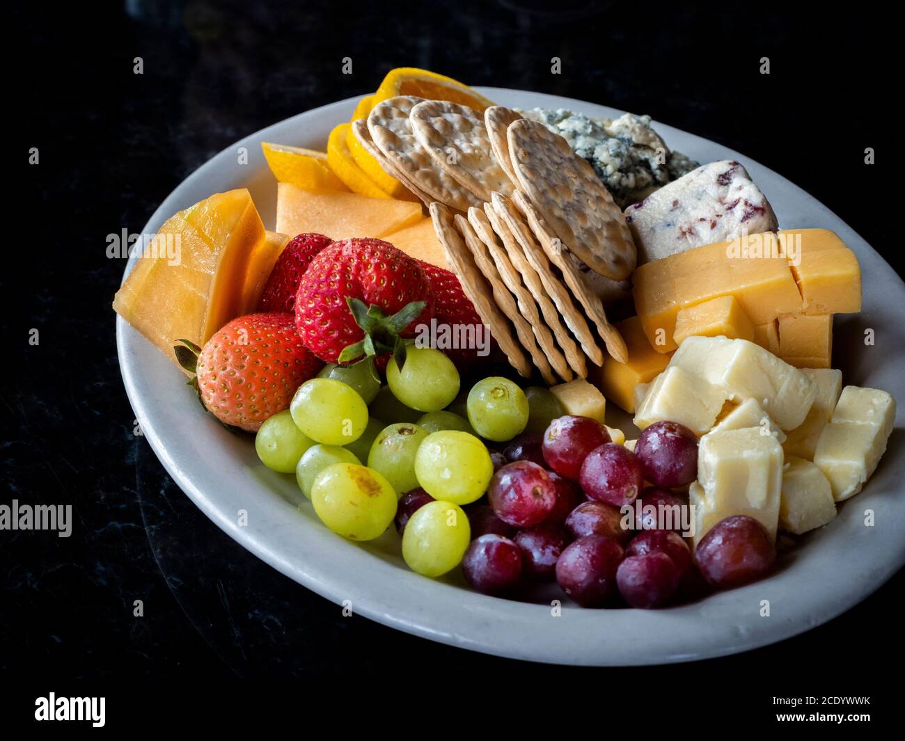 Obstkäse und Cracker und ein Teller auf einem schwarzen Hintergrund Stockfoto