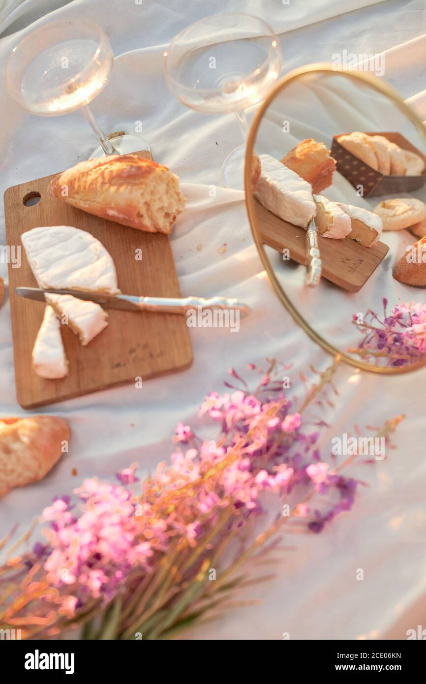 Sommer - Picknick. Käse Brie, Baguette, Pfirsiche, Champagner, Spiegelei, Blumen und Korb Stockfoto