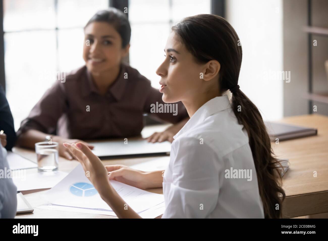 Fokussierte junge arabische Frau im Gespräch mit verschiedenen Teamkollegen. Stockfoto