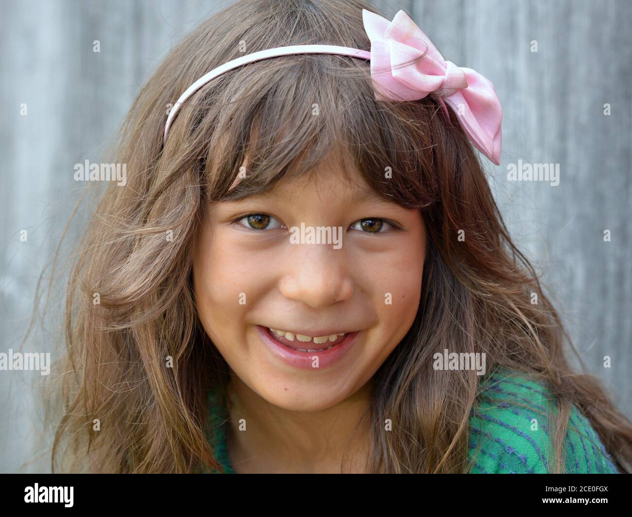 Niedliche kleine gemischte Rasse Tween Mädchen (kaukasischen und ostasiatischen) mit rosa Schleife Knoten Stirnband lächelt für die Kamera. Stockfoto