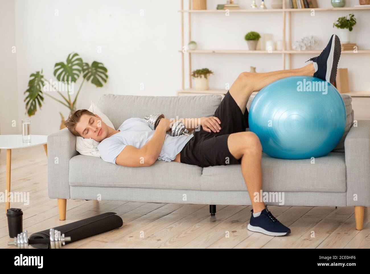 Faulheit und Training. Müde Kerl schlafen auf Couch mit Hantel und Fitness-Ball Stockfoto