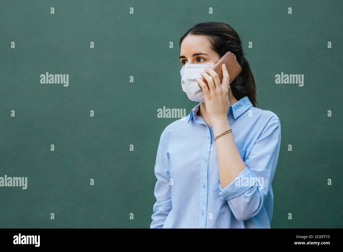 Stock Foto von einer jungen Frau trägt eine Gesichtsmaske Telefongespräch auf grünem Hintergrund und Platz zum Kopieren Auf der linken Seite Stockfoto