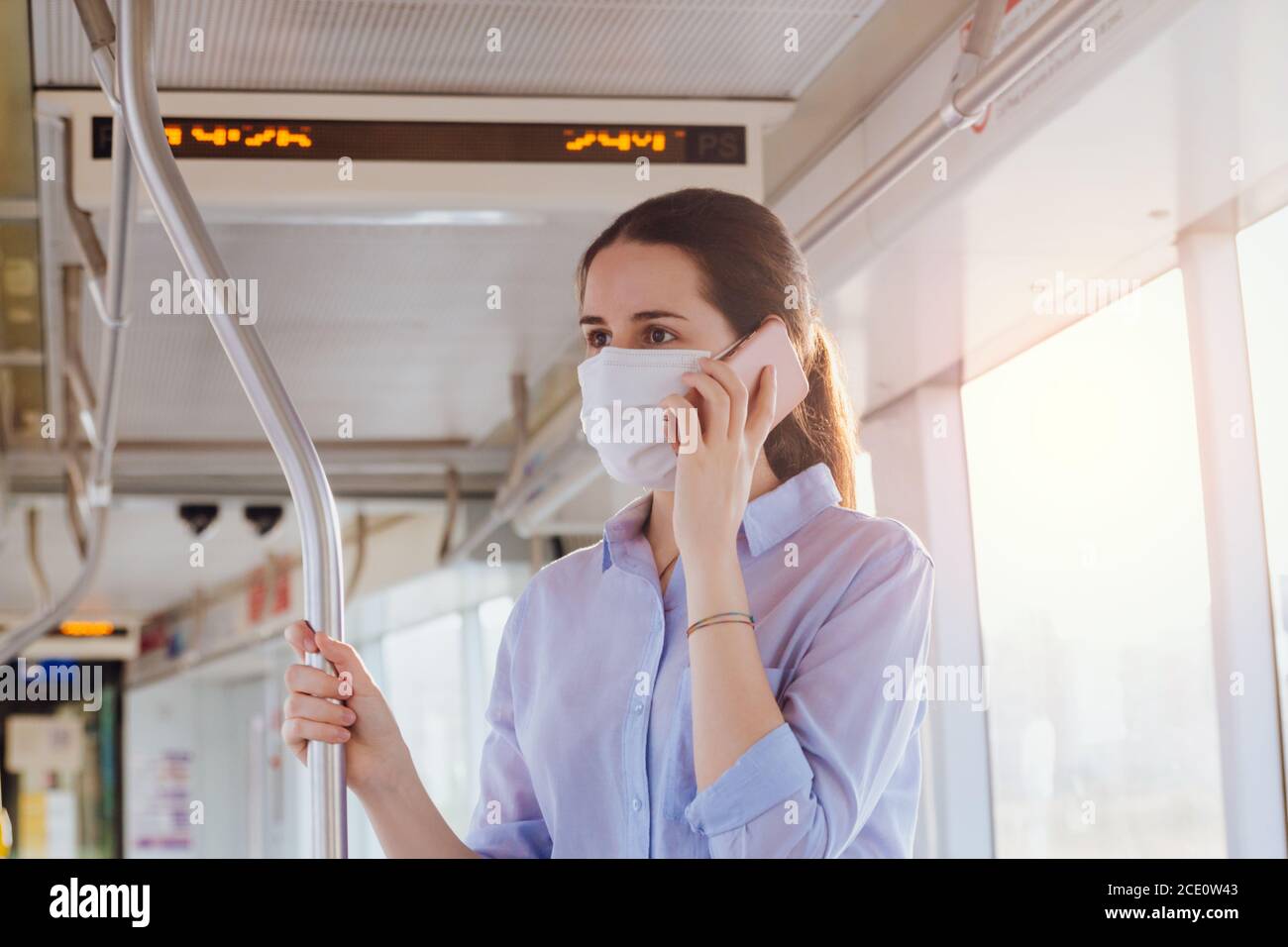 Stock Foto von einer jungen Frau trägt eine Gesichtsmaske Telefonieren im Stehen auf den öffentlichen Verkehrsmitteln Stockfoto