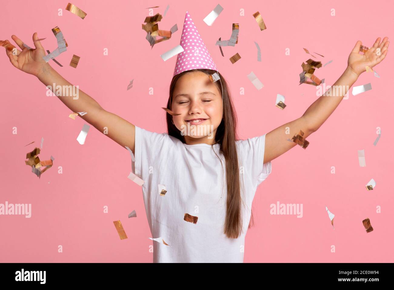 Glück, Unterhaltung und Geburtstag. Aufgeregt Kind mit geschlossenen Augen in festlichen Hut genießen Konfetti Stockfoto