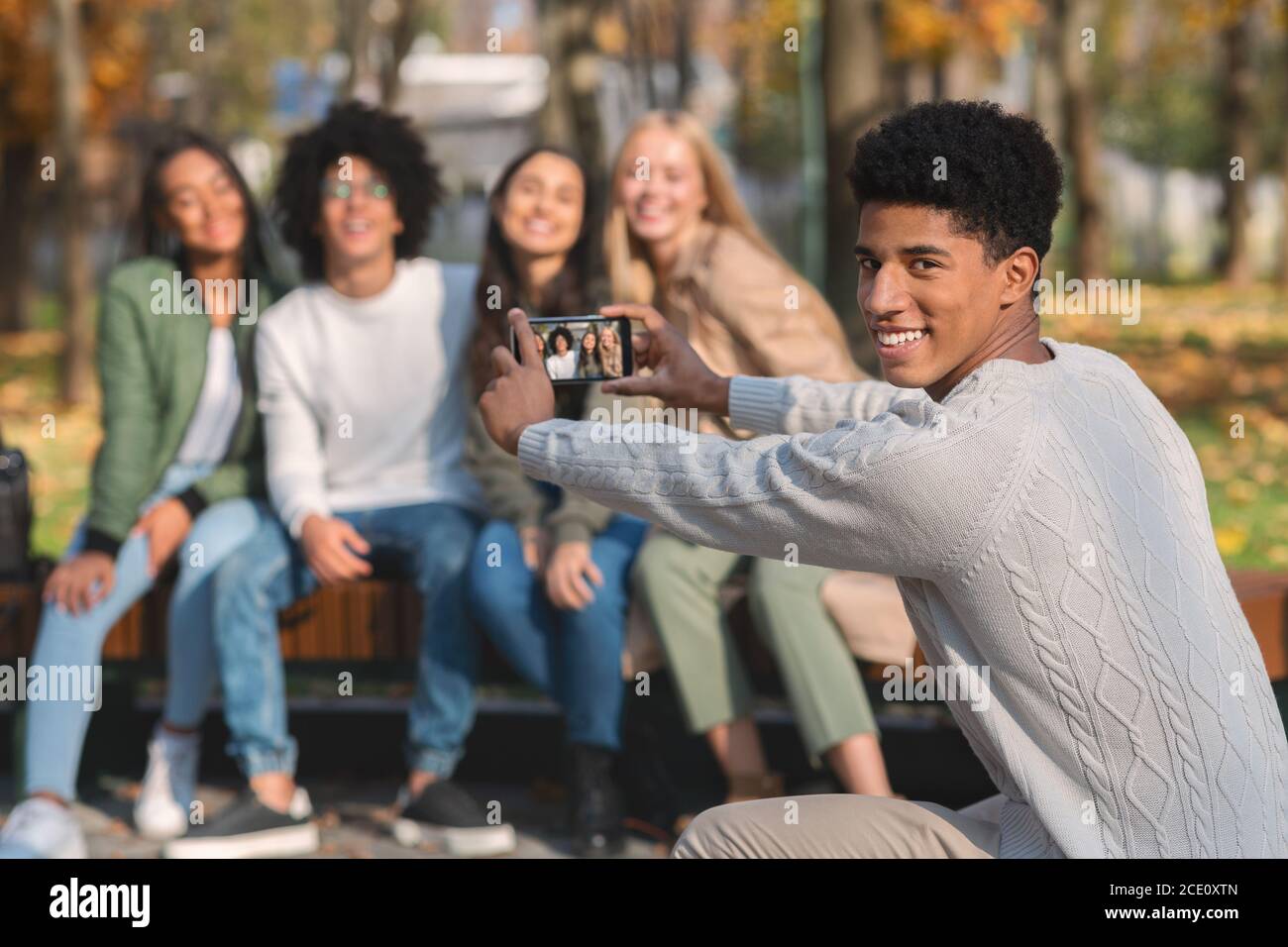 Lächelnder afrikanischer Kerl, der Foto von seinen jugendlich Freunden nimmt Stockfoto