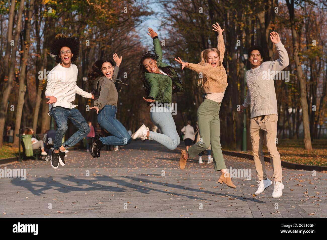 Fröhliche internationale Gruppe von Freunden, die im Park aufspringen Stockfoto